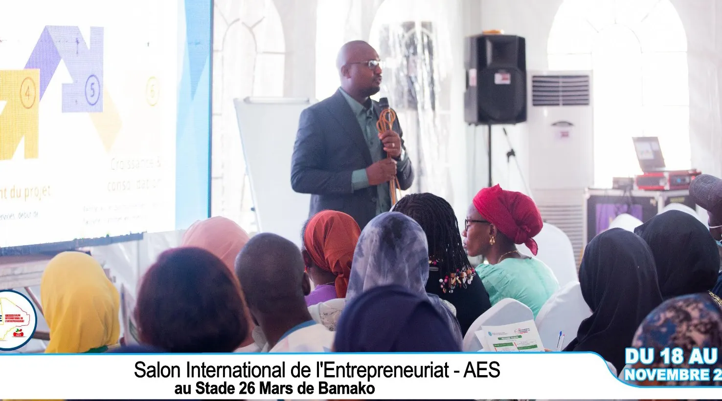 Formateur animant une session devant un public attentif sous la tente